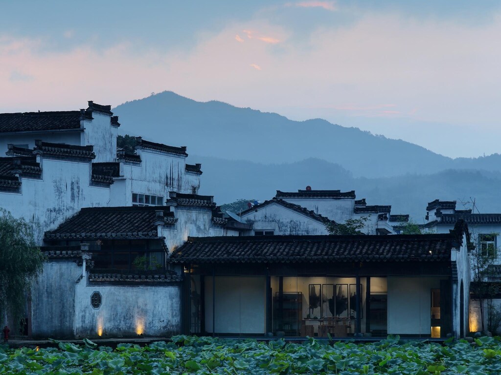 WildChina introduces the Best Boutique Hotels in China (2024) - Su House, with black tiled roofs and white walls, subtly lit at night.