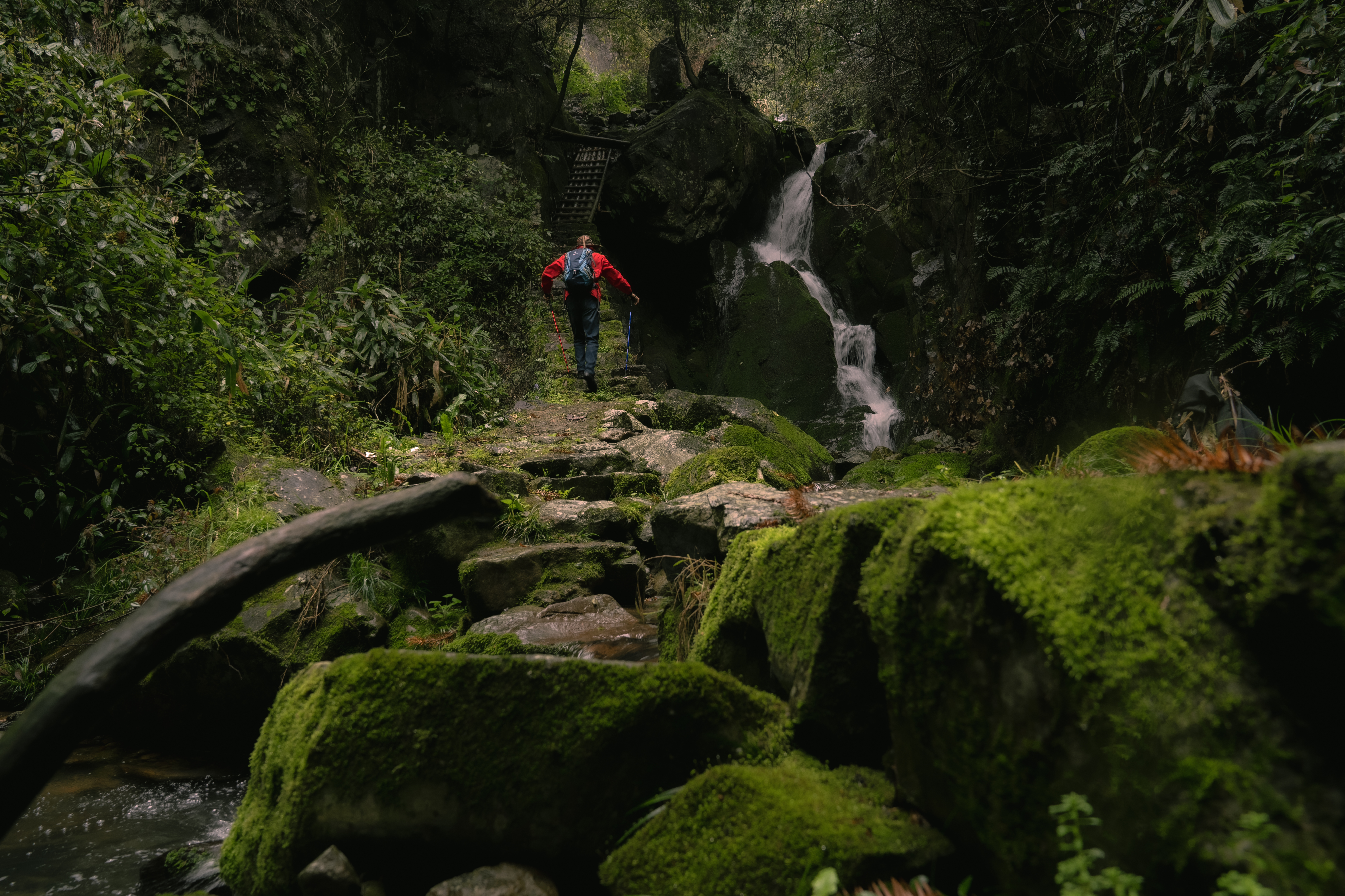 A hiker walking on a stone path next to a waterfall on Songyang ancient trails.